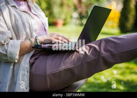La donna sta usando un computer portatile in giardino. Le mani femminili scrivono sul notebook Foto Stock
