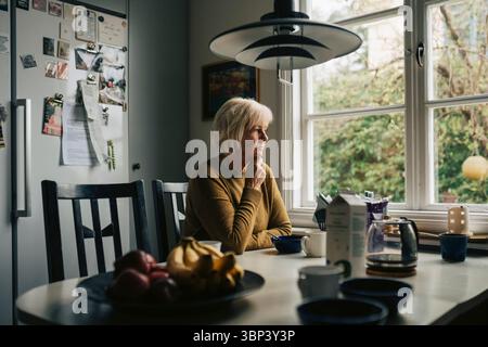 Donna anziana contemplativa seduta a tavola a casa Foto Stock