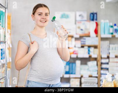 Una donna incinta beve acqua dalla bottiglia mentre fa shopping Foto Stock