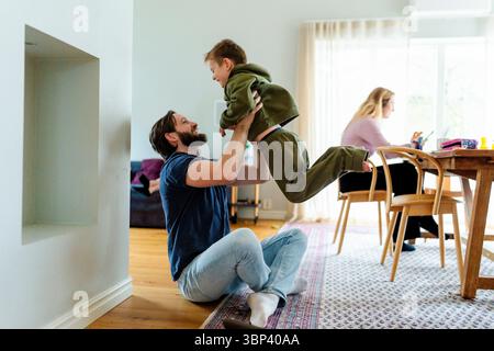 Padre che gioca con il figlio seduto a gambe incrociate sul pavimento di casa Foto Stock