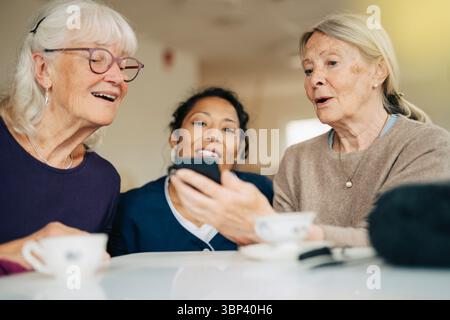 Donna anziana che condivide lo smartphone con un amico e un infermiere a casa di riposo Foto Stock