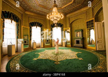Khiva, Uzbekistan - 12 luglio 2024: Interno della sala degli specchi all'interno del Palazzo Nurullabay, Khiva, Uzbekistan, con una donna al centro. Foto Stock