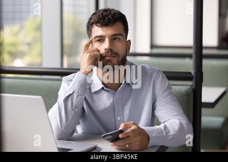 Giovane uomo penoso seduto a tavola a contemplare un messaggio sulla cellula Foto Stock