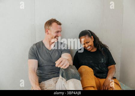 Uomo sorridente che passa il tempo libero con una donna mentre si prende una pausa dalla ristrutturazione della casa Foto Stock