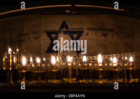 Le candele di petrolio bruciano su una menorah di Hanukkah sullo sfondo di una bandiera israeliana blu e bianca fuori da una casa a Gerusalemme, Israele. Foto Stock