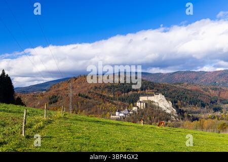 Vista panoramica del Castello di Bobolice, annidato nel fogliame autunnale, con mucche che pascolano pacificamente in primo piano sotto un cielo blu Foto Stock