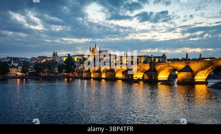 Ponte Carlo illuminato e Castello di Praga al tramonto con acqua riflettente Foto Stock