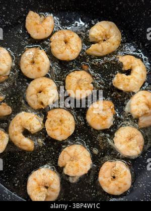 L'immagine mostra la frittura di gamberi sbucciati nell'olio in una padella nera antiaderente. I gamberi sono parzialmente cotti e presentano una cucitura marrone-arancio chiaro, indicata Foto Stock