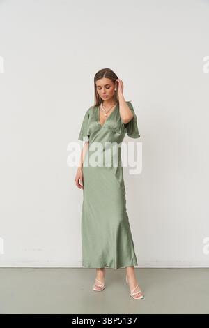 Una bella donna indossa con grazia un abito verde alla moda, che mostra il suo stile elegante in un luminoso ambiente interno studio, irradiando fiducia e. Foto Stock