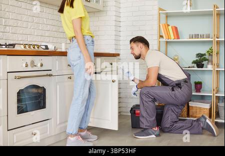 Uomo professionista che fissa problemi con lavandino, scarico intasato, cliente donna in piedi Foto Stock