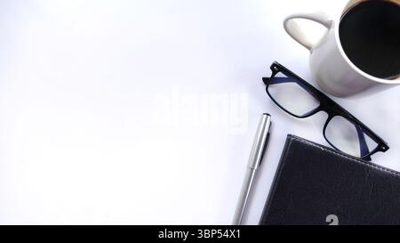 Area di lavoro minimalista con vista, penna, notebook e una tazza di caffè su bianco. Ideale per aziende, pianificazione, produttività, gestione del tempo Foto Stock