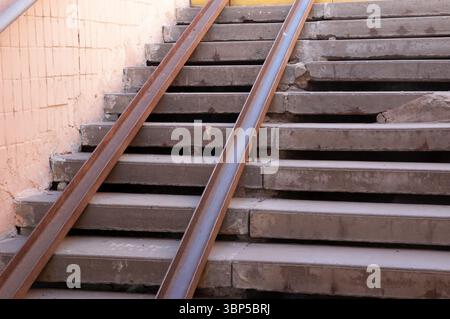 Vecchie scale in cemento in un sottopassaggio, usurate e riparate grossolanamente. Due guide metalliche arrugginite fungono da rampa improvvisata, mostrando segni di decadimento e avvicinamento Foto Stock