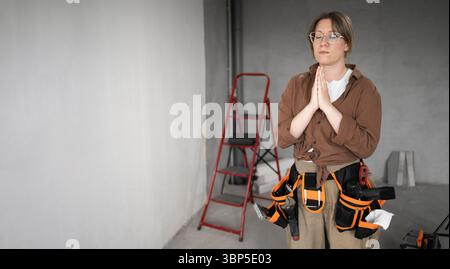 Meditazione e riparazione concetto di casa. Riparatrice professionale in posa meditativa che fa riparazione domestica tenendosi per mano in gesto di preghiera Foto Stock