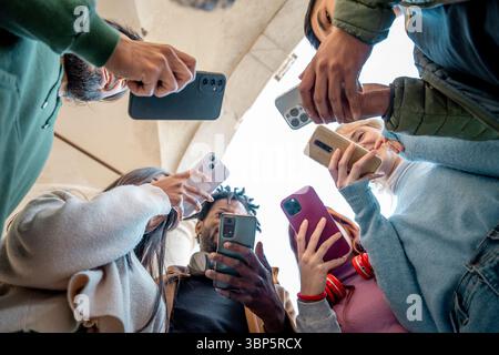 Gruppo di giovani adulti diversi che utilizzano smartphone in cerchio dal basso, rappresentando la connessione digitale, la cultura giovanile e la tecnologia mobile Foto Stock