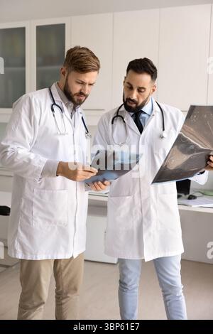 Due giovani medici maschi seri in piedi insieme in ufficio ospedaliero Foto Stock