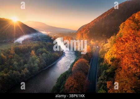 Vista aerea di un fiume tortuoso, di una strada e di una vibrante foresta autunnale Foto Stock