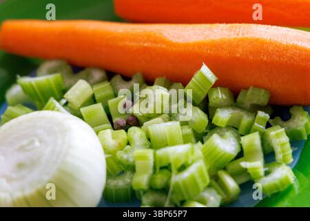 Il piatto verde mostra verdure fresche, tra cui mezza cipolla sbucciata, gambi di sedano tritati e due carote intere. Foto Stock