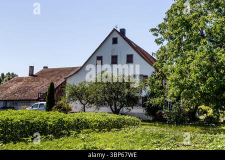 Vecchia fattoria sull'isola monastica di Reichenau. Una doppia croce si erge sul timpano, segno che si tratta di una tenuta feudale appartenente al monastero. La doppia croce è anche un simbolo di protezione divina contro tempeste, fulmini e fuoco. Questa immagine mostra una casa tradizionale con giardini e campi vicini a Hochwartstraße, sull'isola di Reichenau nel Baden-Württemberg, in Germania. La doppia croce sul tetto indica il suo status originale di feudo. Trasmette un'impressione della vita rurale e del carattere agricolo del sito patrimonio dell'umanità dell'UNESCO. Hochwartstraß Foto Stock