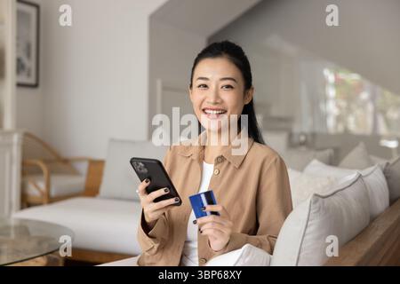 Ritratto di donna che guarda la fotocamera che tiene la scheda e lo smartphone Foto Stock