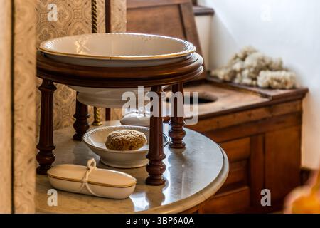 Uno storico lavandino con vaschetta, spugna e sapone si erge su un tavolo di marmo. Sullo sfondo si può vedere una toilette in legno asciutta. Questo arredamento illustra le condizioni igieniche personali di un tempo al castello di Arenenberg a Salenstein, in Turgovia, in Svizzera Foto Stock