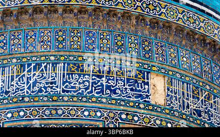 Primo piano di intricate piastrelle islamiche con motivi geometrici colorati e calligrafia araba. Il design presenta blu, gialli e vivaci Foto Stock