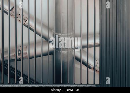 Le colonne e le travi in acciaio creano un motivo intricato, visibile attraverso le barre verticali di una griglia in un ambiente industriale Foto Stock