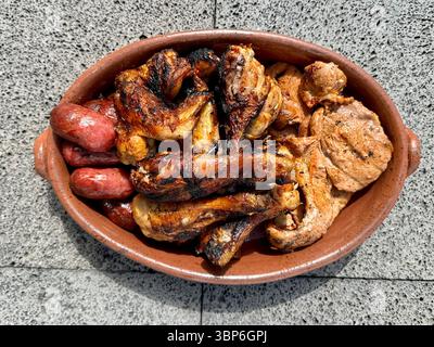Piatto misto di carne alla griglia servito in un piatto di terracotta, con ali di pollo, costolette di maiale e salsicce. Foto Stock