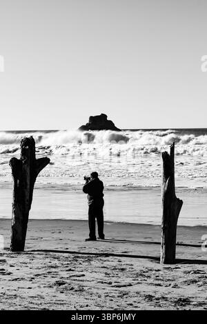 Arch Cape, Oregon - 26 novembre 2015: Un fotografo cattura la potenza dell'oceano, incorniciato da una deriva, cercando lo scatto perfetto delle onde che si infrangono Foto Stock