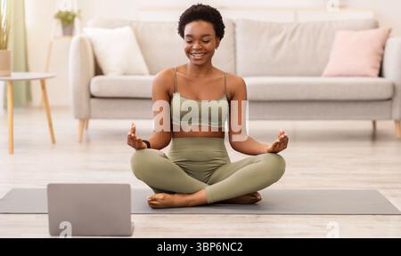 Felice donna nera che meditava seduta al laptop a casa Foto Stock