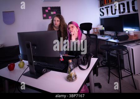 Due donne sono incentrate sullo schermo di un computer desktop, lavorando insieme in un ambiente moderno ed elegante, mostrando lavoro di squadra e collaborazioni Foto Stock
