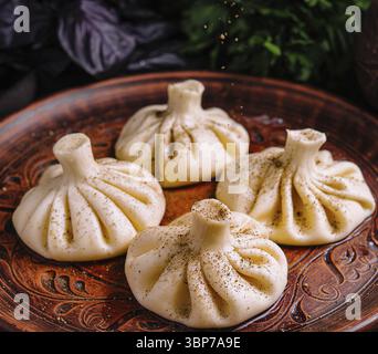 Cibo, gnocchi tradizionali georgiani, khinkali, serviti su un piatto di legno intagliato con erbe fresche Foto Stock