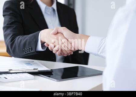Primo piano di una stretta di mano professionale tra colleghi che concludono un affare, con documenti di lavoro e tablet in background Foto Stock