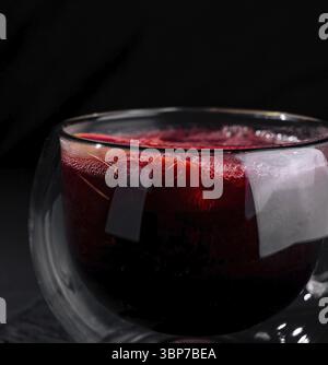 Cibo, Una moderna tazza di vetro a doppia parete piena di tè rosso, isolata su uno sfondo scuro e umido Foto Stock