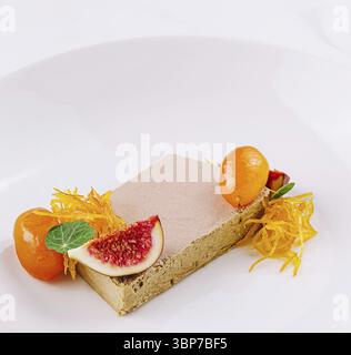 Cibo, fetta di foie gras viene servita su un piatto bianco, guarnita con fichi, kumquat e fiori commestibili Foto Stock