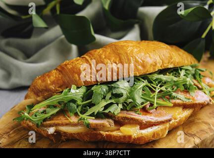 Cibo, delizioso panino con croissant ripieno di pancetta, rucola e formaggio su un tavolo di legno Foto Stock