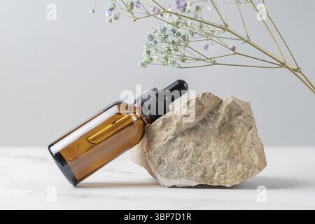 Faccia il siero o l'olio essenziale in bottiglia del contagocce di vetro scuro vicino alla pietra ed al ramo essiccato del fiore della gypsophila. Presentazione del prodotto cosmetico per la cura della pelle Foto Stock