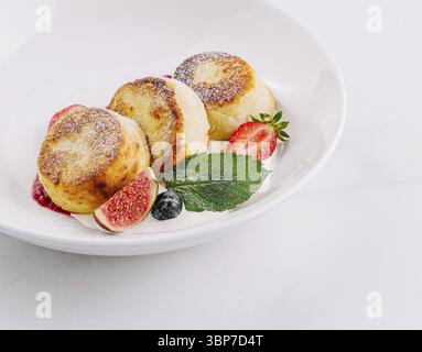 Cibo, tre frittelle di formaggio dorato guarnite con fragole e menta su un piatto bianco Foto Stock