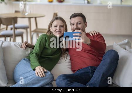 Una coppia felice e felice che guarda la fotocamera del telefono, fa videochiamate con gli amici, fa selfie su smartphone, crea un'immagine del profilo per i social Foto Stock