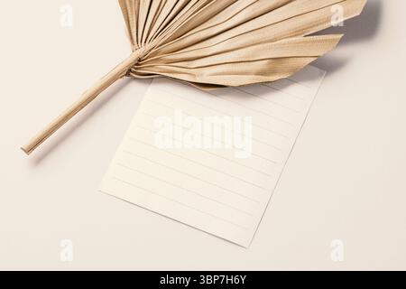 Mock-up di carta in colori neutri. Carta vuota e foglie di palmo essiccate. Composizione piatta, spazio per il testo Foto Stock