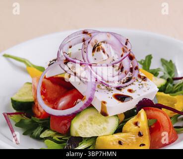 Cibo, insalata greca colorata e sana con formaggio feta. Verdure fresche. E verdi verdeggianti su un piatto bianco. Un vegetariano delizioso e nutriente Foto Stock