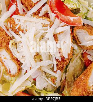 Cibo, Un'insalata abbondante con croccanti strisce di pollo su un letto di lattuga fresca e vivaci peperoni rossi, abbondantemente conditi con formaggio rasato per l'aggiunta Foto Stock