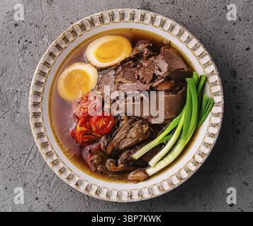 Cibo, tradizionale ramen di manzo con uova sode, pomodori e cipolle verdi in un ricco brodo Foto Stock
