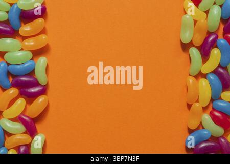 Jelly Beans assortiti bordo con copyspace su sfondo arancione Foto Stock