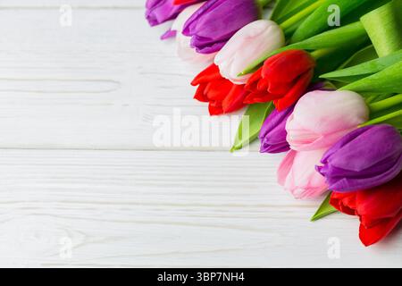 Il bouquet di vibranti steli di tulipani si trova diagonalmente su una superficie di legno verniciata di colore bianco Foto Stock