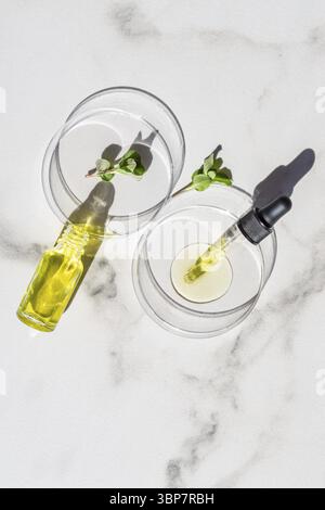 Pipettare il siero cosmetico su una piastra Petri con foglie di menta verde su sfondo di marmo bianco. Concetto di cosmetologia e farmaceutica. Peeling acido, viso Foto Stock