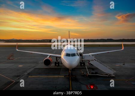 Aereo di linea commerciale parcheggiato sull'asfalto all'alba sotto un bellissimo cielo colorato all'aeroporto internazionale di Milano Malpensa in Italia. Foto Stock