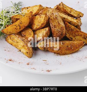 Cibo, patate arrosto dorate condite con spezie, guarnite con erbe su sfondo bianco Foto Stock