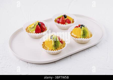 Cibo, eleganti tartette con kiwi, arancia e fette di fragola su un piatto di ceramica Foto Stock