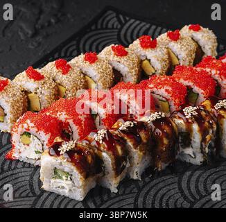 Cibo, lussuoso assortimento di sushi roll disposti artisticamente su un elegante piatto nero con sfondo testurizzato Foto Stock