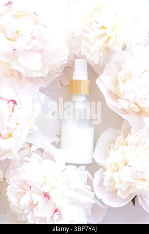 Bottiglia di crema bianca e sfondo di fiori di peonia. Confezione in vetro smerigliato bianco prodotto cosmetico per la cura della pelle. Bottiglia bianca di lozione senza marchio, balsamo, mano Foto Stock